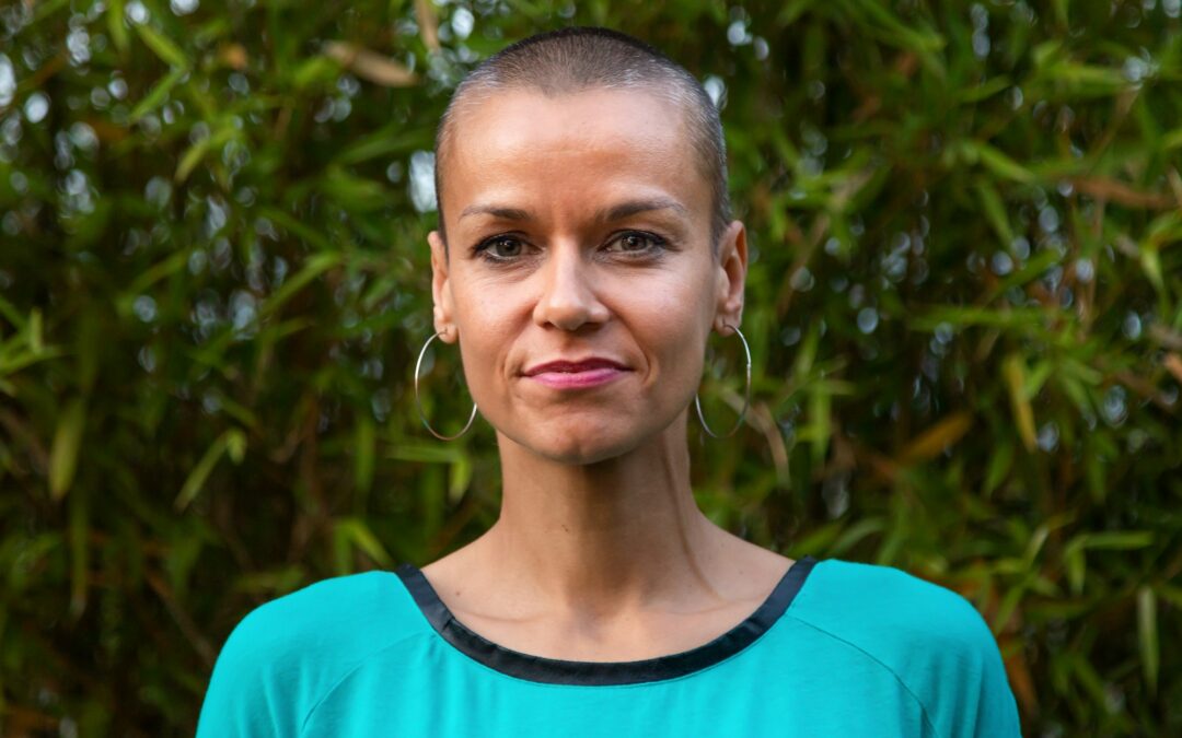 Horizontal headshot of adult caucasian woman in nature with big earring hoops and buzz haircut.